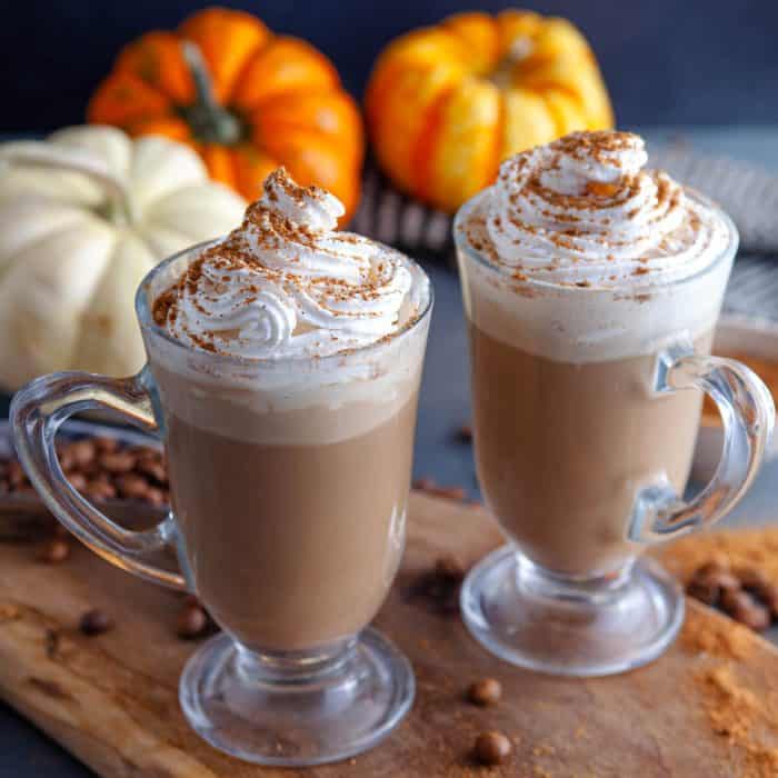 two cups of pumpkin spice irish coffee topped with a generous dollop of whipped cream and a sprinkle of spice
