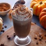 pumpkin spice irish coffee in a glass placed in a wooden board with coffee beans and pumpkins on the table