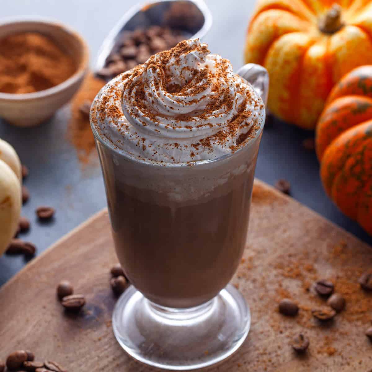 pumpkin spice irish coffee in a glass placed in a wooden board with coffee beans and pumpkins on the table