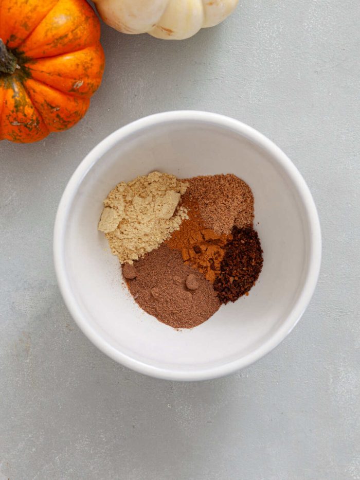 cinnamon, ginger, nutmeg, allspice, and cloves in a white mixing bowl