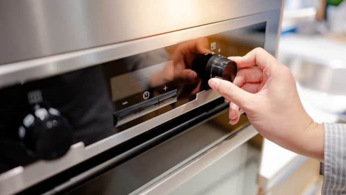 Male hand turning temperature knob of modern oven in kitchen showroom