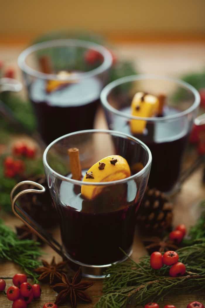 Mulled wine in glass mugs decorated with lemon slices studded with cloves on wooden table, red berries and evergreen sprigs, selective focus
