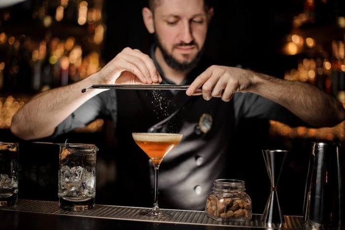 Male bartender adding to a cocktail in the glass a grated nutmeg