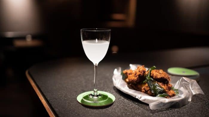 Crispy fried chicken wings and a glass of drink on a bar counter
