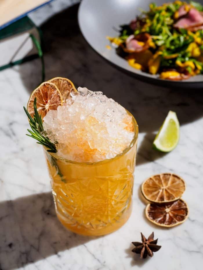 Orange cocktail with crushed ice and rosemary, salad on a background