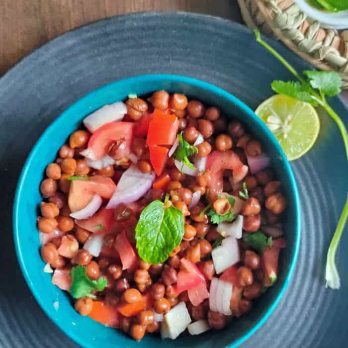 a teal-colored bowl full of kala chana chaat with lime on the side