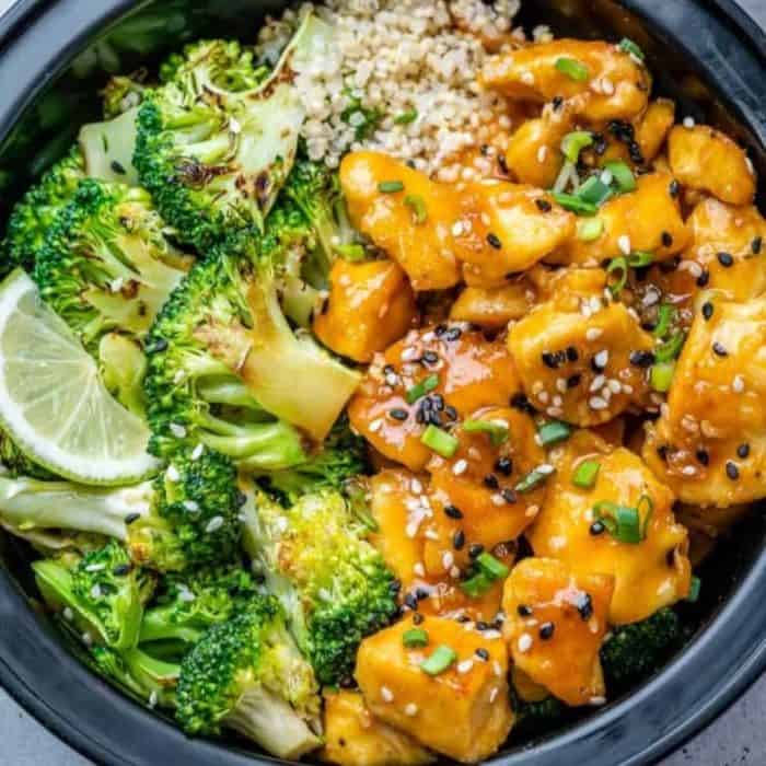a black plate full of honey garlic chicken, broccoli, and rice
