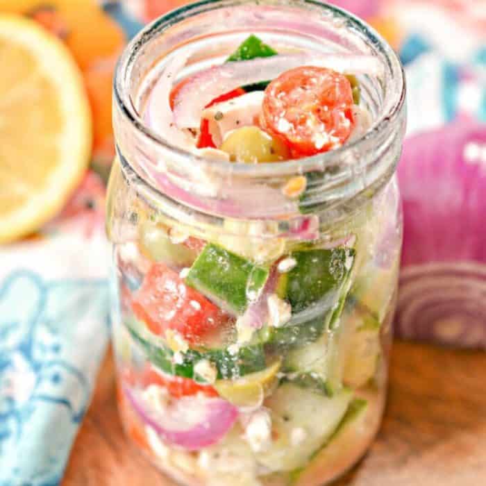 a jar full of greek salad with a slice of orange and onion on the side