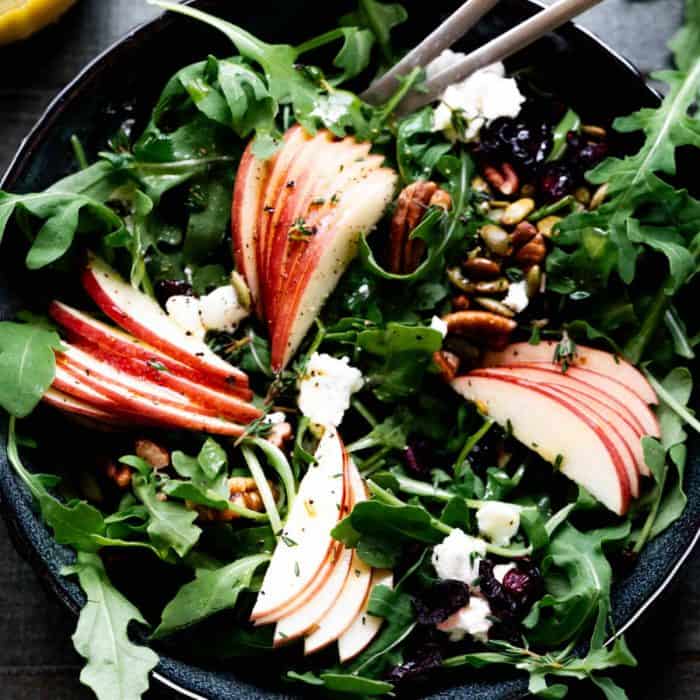 a black bowl filled with Arugula Apple Salad With Goat Cheese