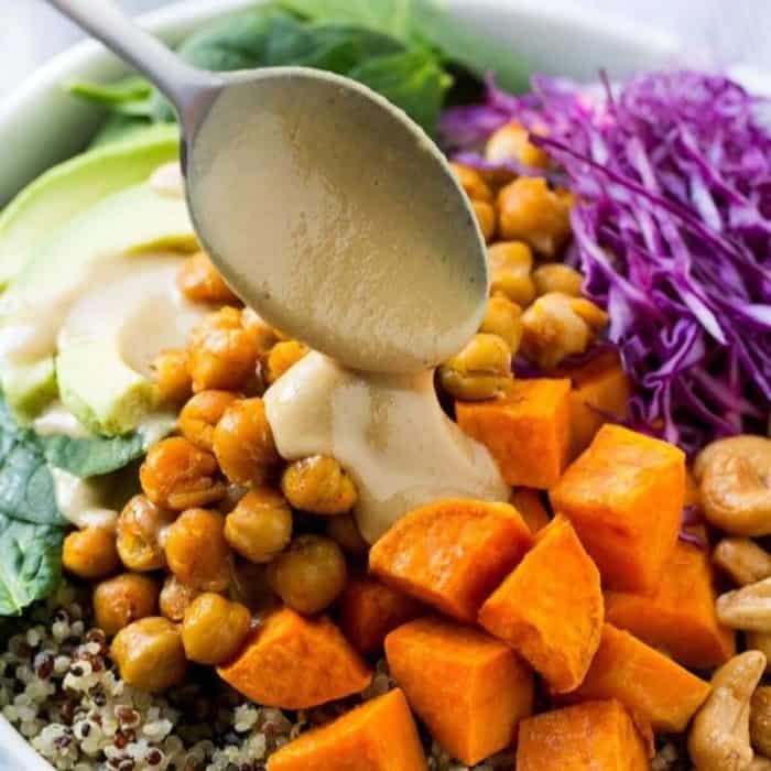 a close up photo of a buddha bowl with a spoon pouring tahini sauce on the top