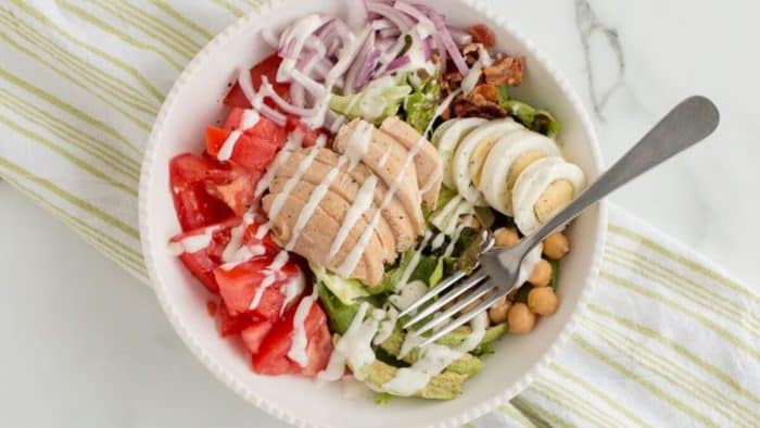 a bowl full of chicken cobb salad with a fork on the side