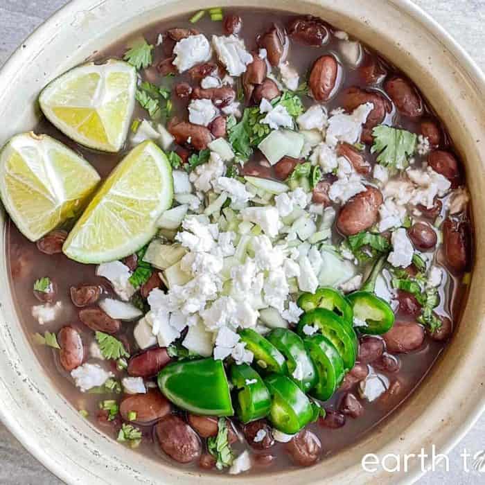 a bowl full of frijoles de la olla with slices of limes on the top