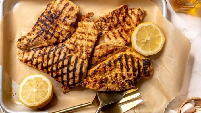 5 pieces of honey lemon garlic chicken with two slices of lemons and fork on the side placed on a wooden board