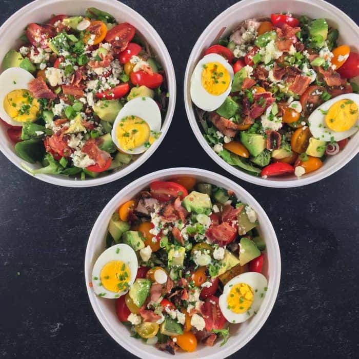three pieces of cobb salad on a bowl placed on a black table