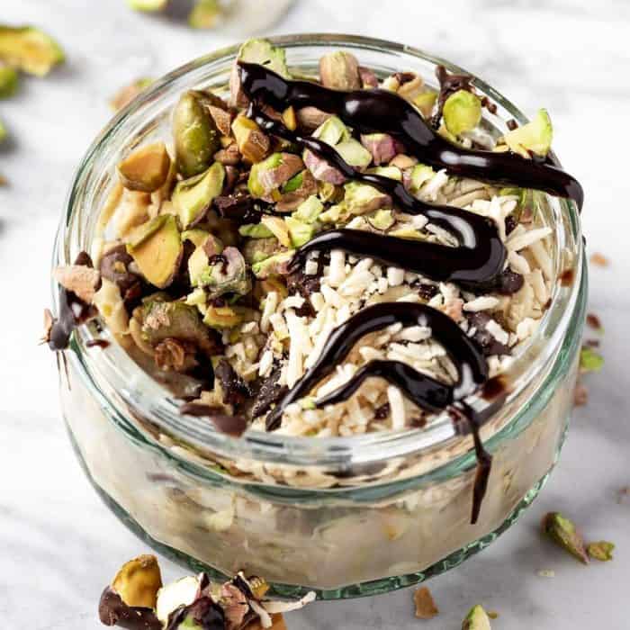 a photo of pistachio overnight oats in a glass jar with chocolate syrup on the top