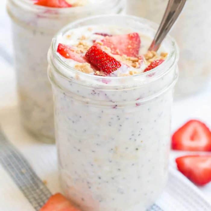 a photo of a jar of strawberry cheesecake overnight oats with strawberry fruits on the top and a spoon