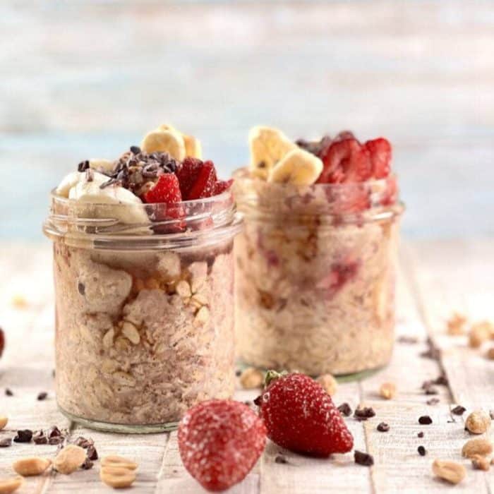 a photo of two jars of peanut butter overnight oats on a wood surface with strawberry fruit on top