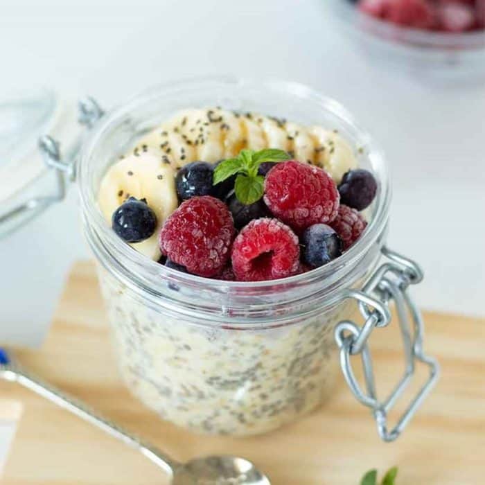 a photo of overnight oats in a jar placed on a wooden chopping board with spoon on the side