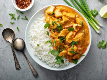 a plate of Chicken and cashew red curry with white rice and green onions on the sides