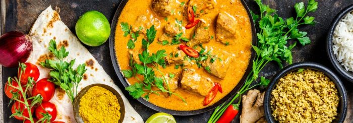 Traditional curry and ingredients on dark background. Curry, lime, ginger, chili, naan bread, rice, couscous, herbs and spices Flat lay