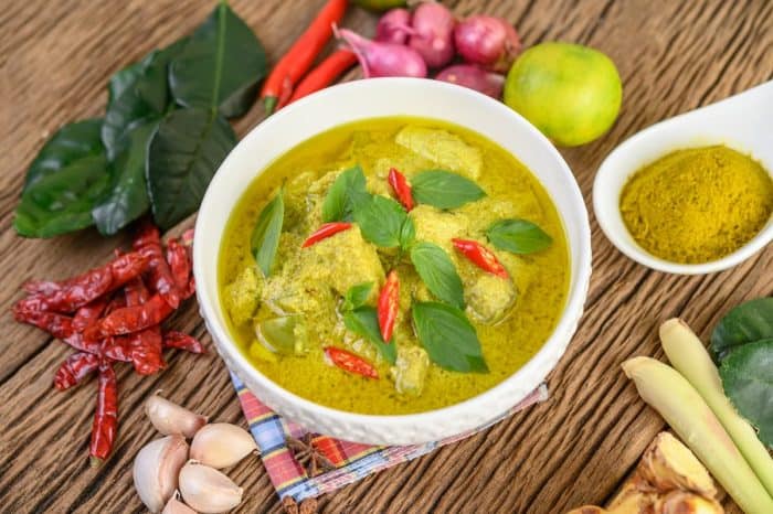 Green curry in a bowl and spices on wooden table