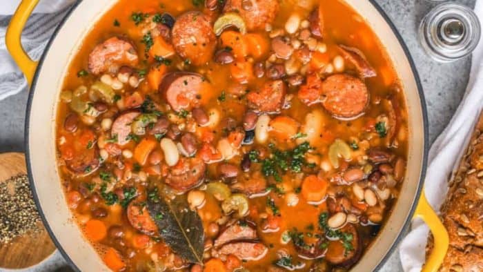 a photo of bean soup with smoked sausage on a white casserole