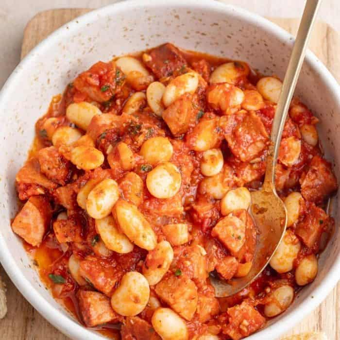 a photo of smoked sausage recipe polish beans and sausage on a white bowl