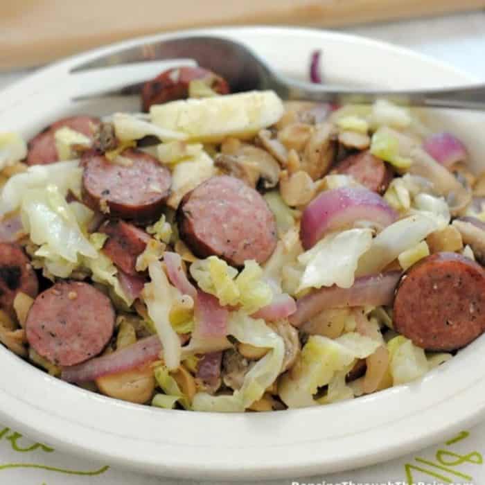 a plate full of smoked sausage and cabbage saute
