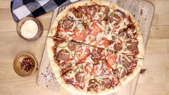 a photo of smoked sausage pizza on a wood surface