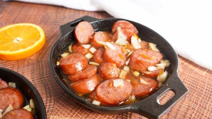 a photo of orange marmalade and bourbon smoked sausage on a small pan with a slice of orange on the side
