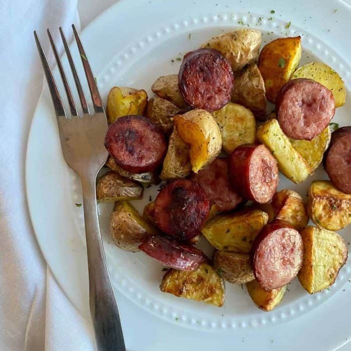 a photo of smoked sausage and potatoes on a white plate with a fork on the side