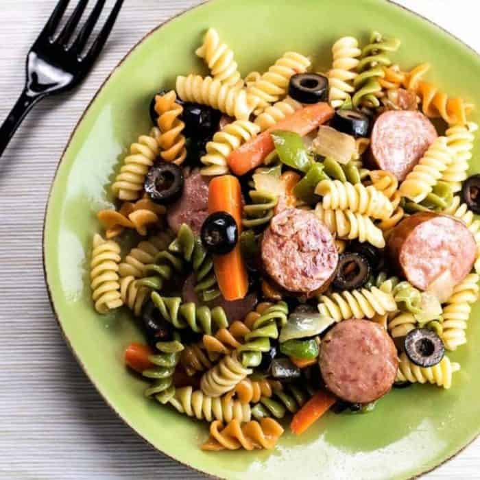 a photo of smoked sausage pasta salad on a green plate with black fork on the side