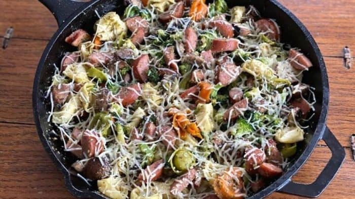 a photo of smoked sausage and tortellini skillet on a black pan on top of a wooden table