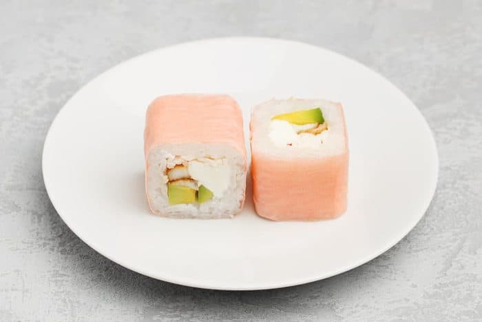 Two pieces of sushi roll in soy paper with eel, avocado and cream cheese on white plate over gray concrete background. Close up view