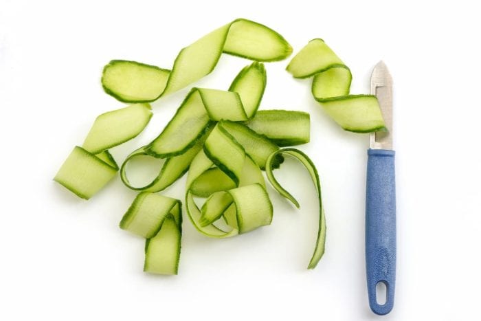 Peeler knife and cucumber shavings on white