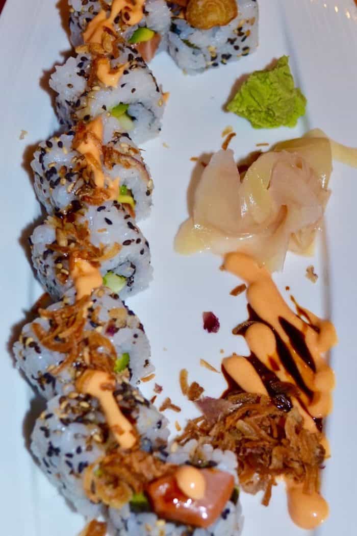 Sushi roll salmon with avocado and cucumber topping with deep fried garlic, Cheesy sauce, pickle ginger and wasabi on side dish
