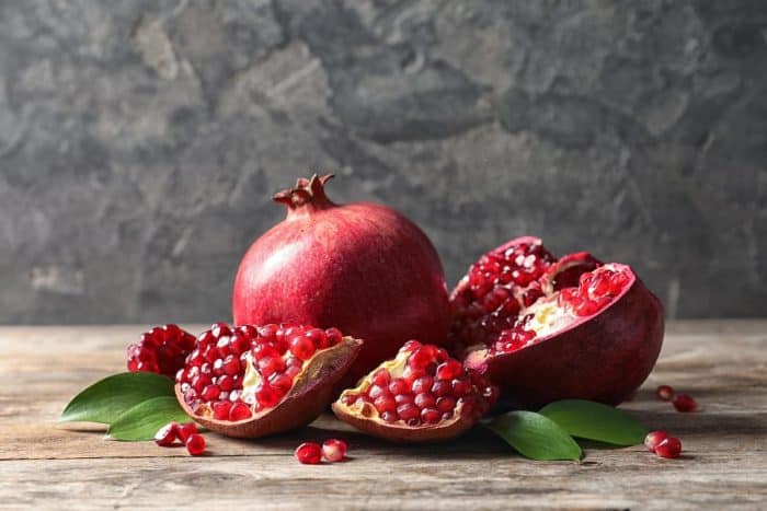Ripe pomegranates and leaves on table against grey background