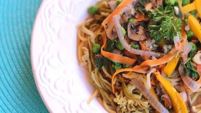 a close up photo of vegan Primavera with Eggplant Noodles on a plate placed on a blue table