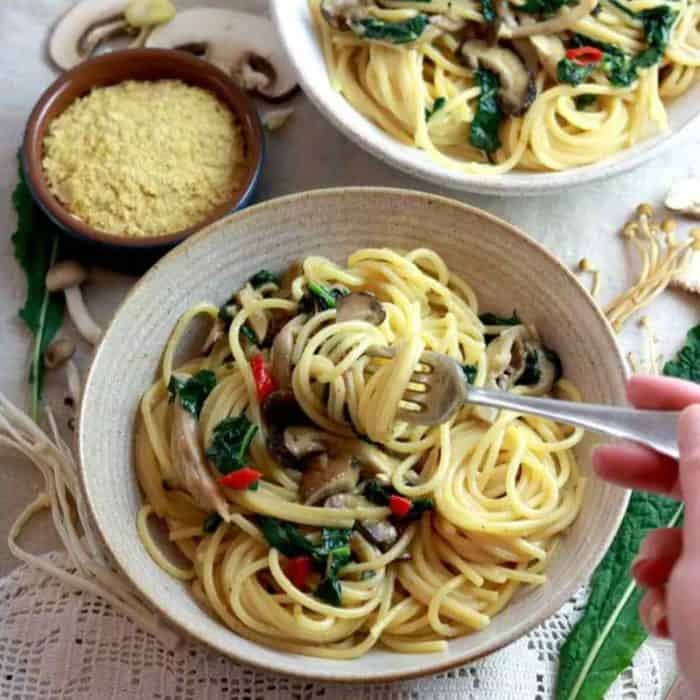 a woman holding a fork and having it rolled on Vegan Smoked Garlic & Wild Mushroom Pasta