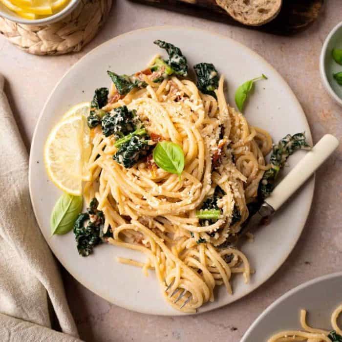 a photo of Cavolo Nero Pasta on a white round plate with slices of lemon and fork on the sides