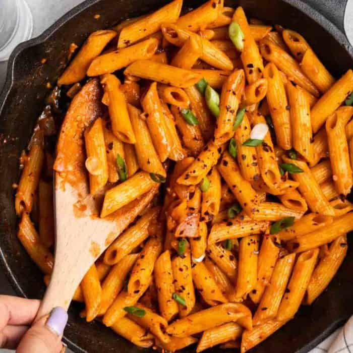 a woman's hand holding a spatula onto a Creamy Korean Gochujang Pasta in a pan