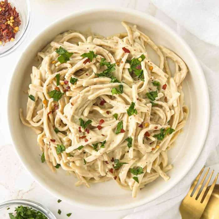 a photo of creamy Silken Tofu Pasta Sauce placed on a round white plate with gold fork on the side