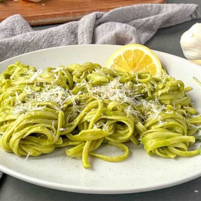 a photo of Trenette al Pesto on a white plate topped with parmesan cheese with a slice of lemon on the side