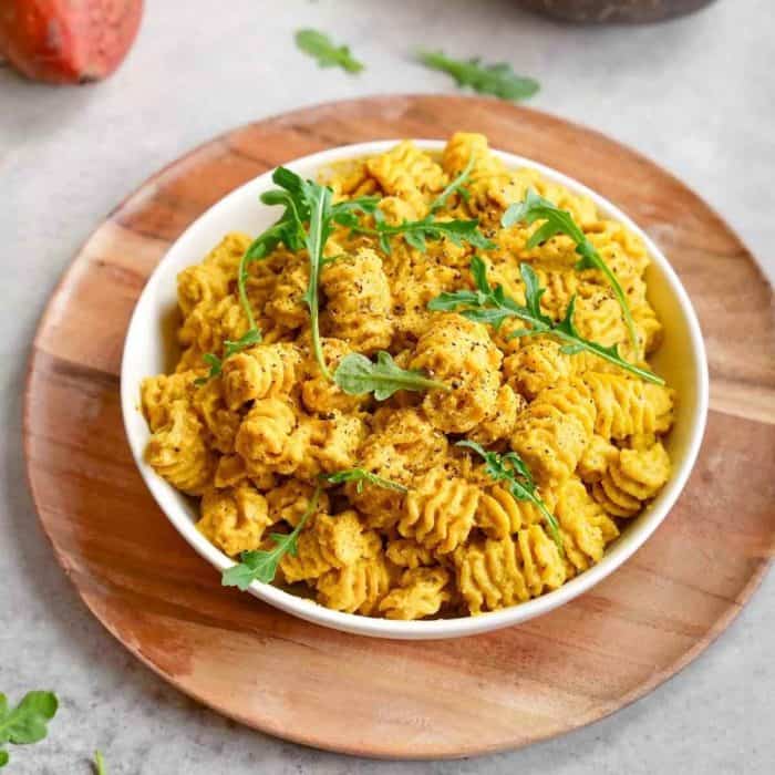 a plate of vegan Creamy Golden Beet Pasta on top of a round wooden board