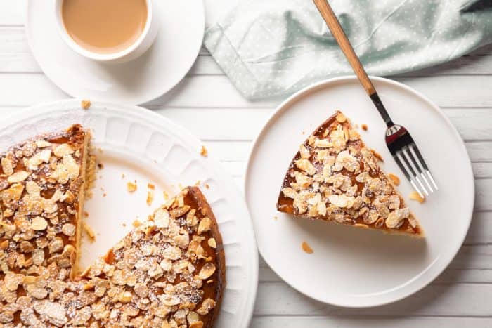 Almond and lemon cake with sliced almonds topping and a coffee cup on a white wooden table.