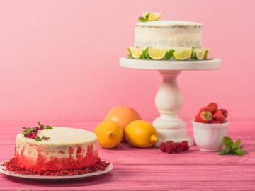 Cake decorated with currants and mint leaves near fruits and white cake on pink wooden surface isolated on pink