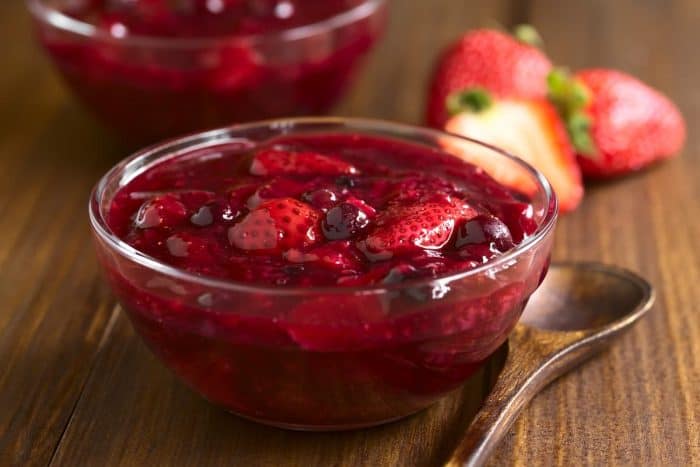German Rote Gruetze (red groats) red berry pudding made of strawberry, blueberry, raspberry and redcurrants cooked with sugar and starch, photographed on wood with natural light