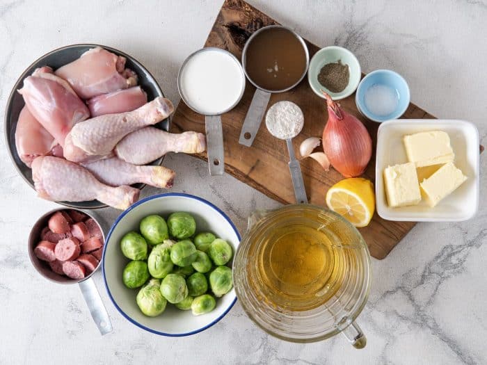 ingredients placed carefully on a marble table such as the chicken legs, seasonings, brussels, broth and butter