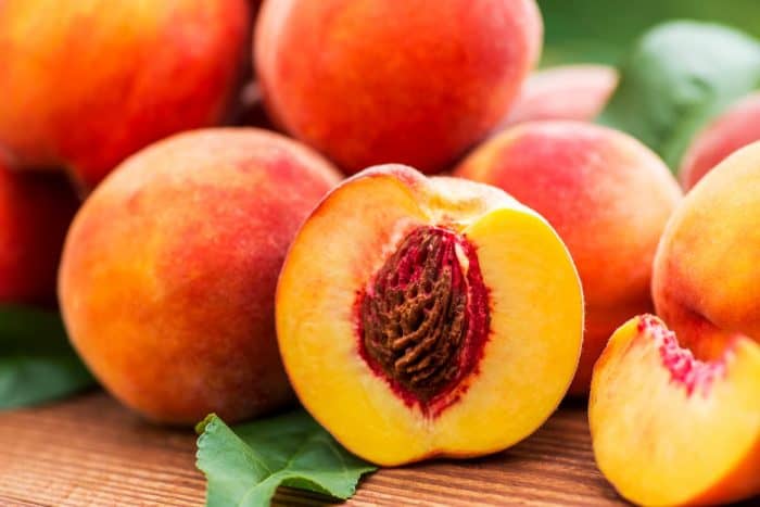 a bunch of fresh peach placed on a wooden table with leaves