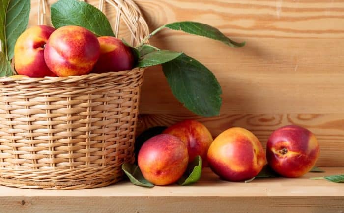 Nectarines with leaves in a wicker basket on a wooden table